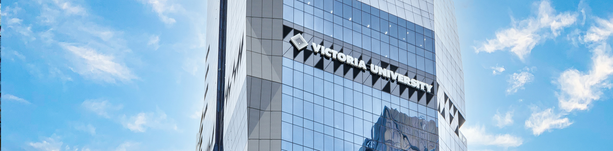 Top of a glass high-rise building with a Victoria University sign