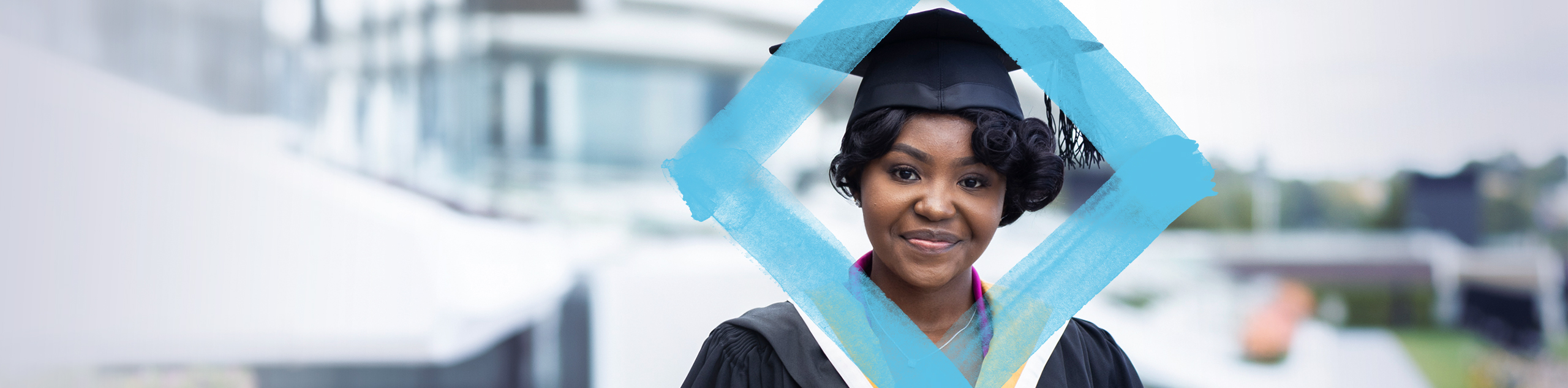 A VU student wearing the graduation gown and hat smiles into the camera, with the floating VU branded diamond.