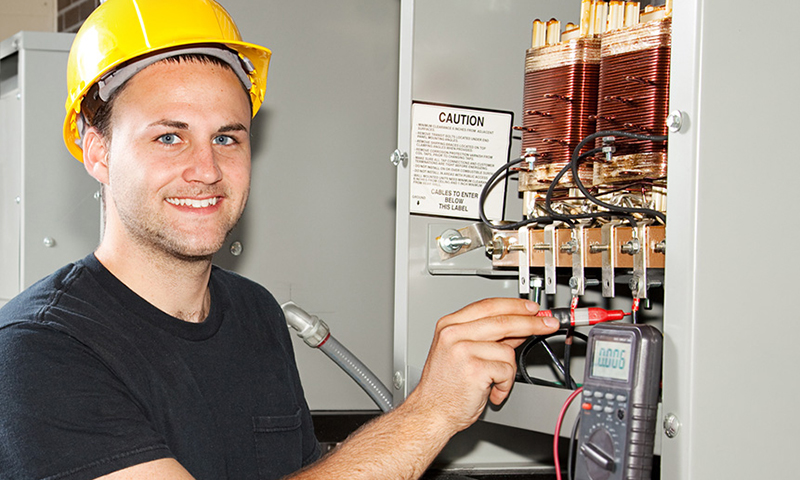 A young man in a hardhat works at an electrical circuit board