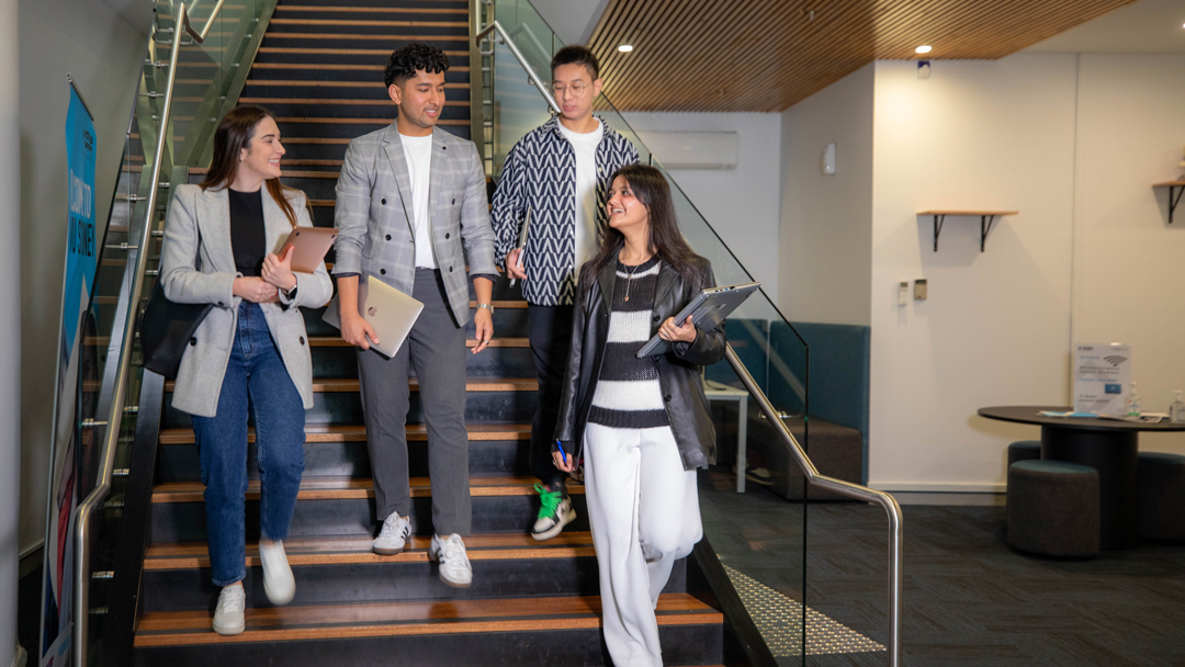 Univerity sudents walk down a campus staircase, carrying books and laptops