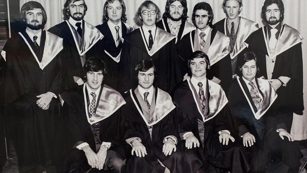 A group of 20-something men in graduation gowns with 1070s facial hair