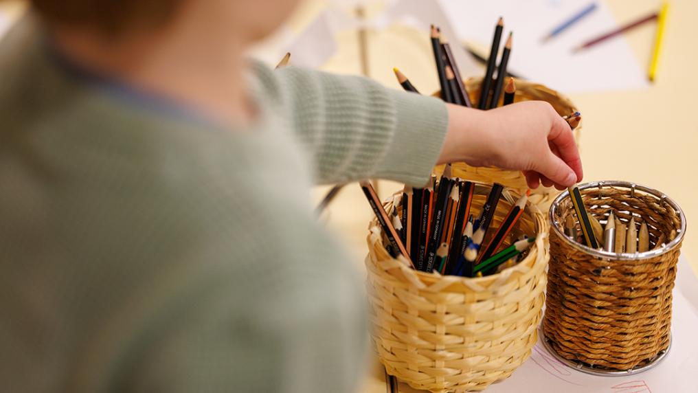 A young boy reaching for a pencil at childcare.