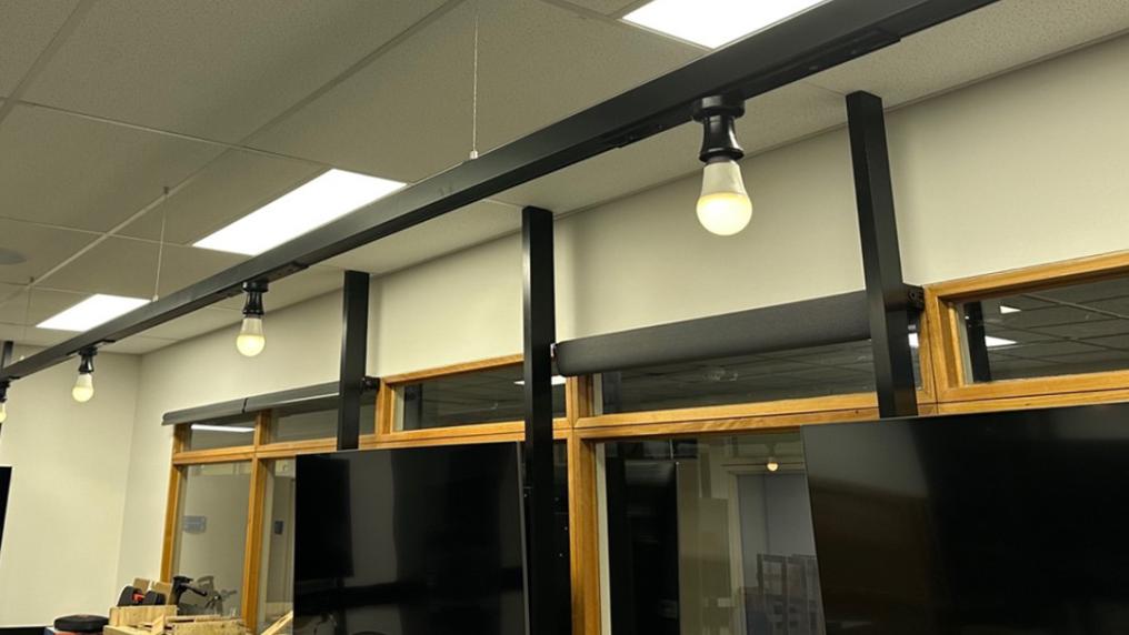 Four lightbulbs attached along a long black beam hanging from the ceiling. The lightbulbs are turned on.